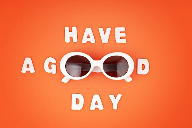 Stylish sunglasses over orange wall with text Have a good day. Summer fashion, party, summertime style, vacations concept. Minimal flat lay, top view