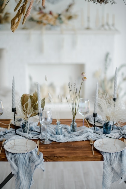 Стильная сервировка с сухоцветами. Тарелка с старинные золотые вилка и нож, свечи, пыльные голубые салфетки на деревянный стол. Зимние свадебные украшения.