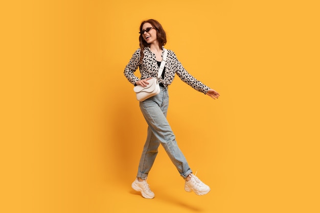 Stylish teen woman in casual outfit and trendy sunglasses posing on yellow