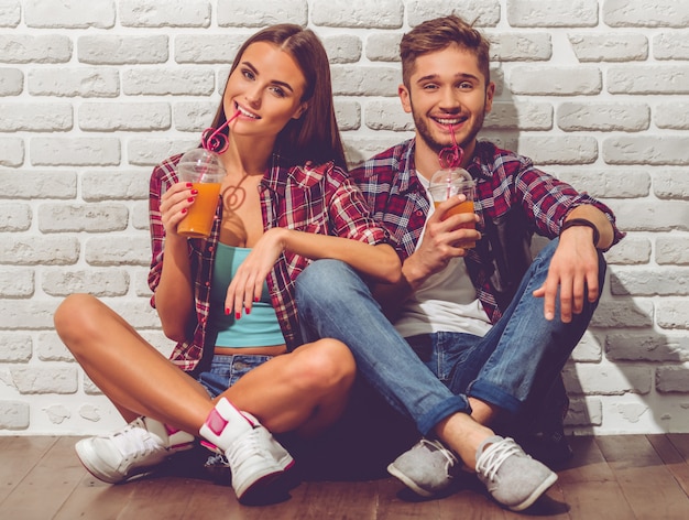 Stylish teenage couple in casual clothes is drinking juice.