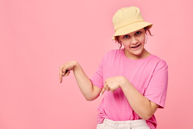 スタイリッシュなティーンエイジャーの女の子モデルのファッション服帽子ピンクのTシャツの装飾ポーズ