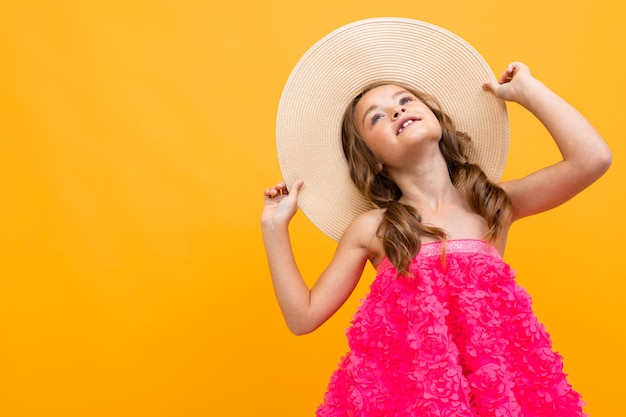 Stylish teenager girl in a pink blouse with a straw hat on her head on a yellow studio background