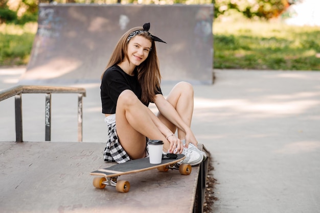 Stylish teenager girl with skateboard sitting and chilling in the skaters park