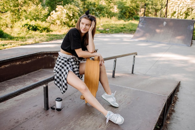 Stylish teenager girl with skateboard sitting and chilling in the skaters park