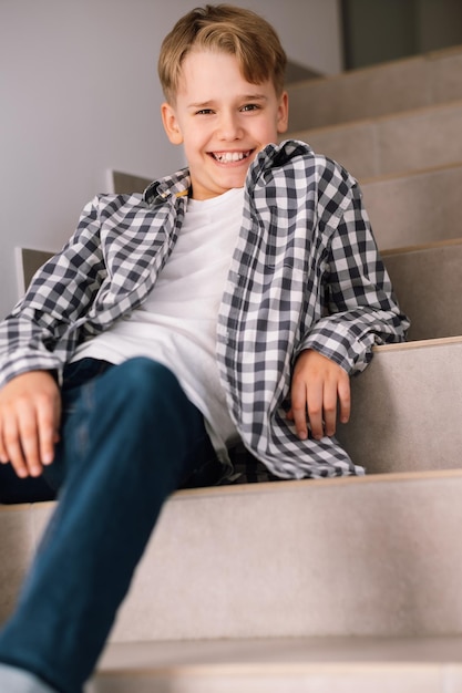 Stylish teenager laughs while looking at the camera The guy is sitting on the steps indoors