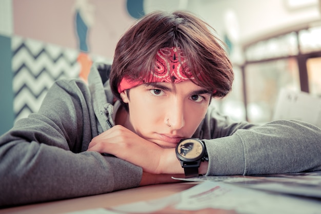 Stylish teenager. Teenager wearing a bandanna and a watch putting his head on hands