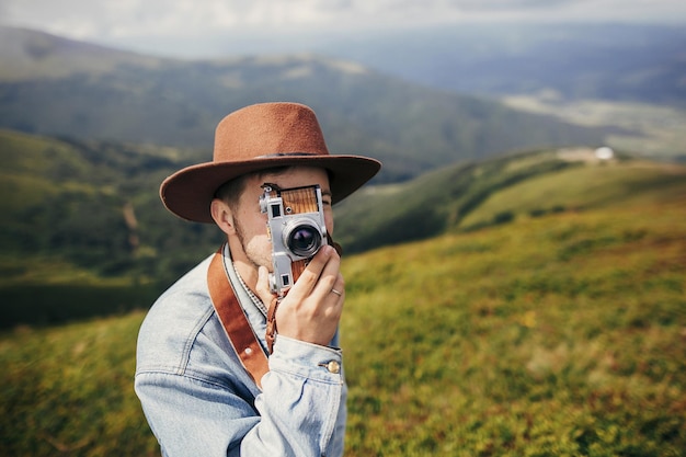 Стильный путешественник, мужчина в шляпе, фотографирующий на вершине горы с местом для фотокамеры для текста, парень-хипстер, путешествующий, делающий снимки удивительных атмосферных моментов путешествий и страсти к путешествиям