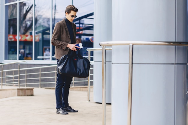 Stylish traveller in jacket with passport and tickets in urban context