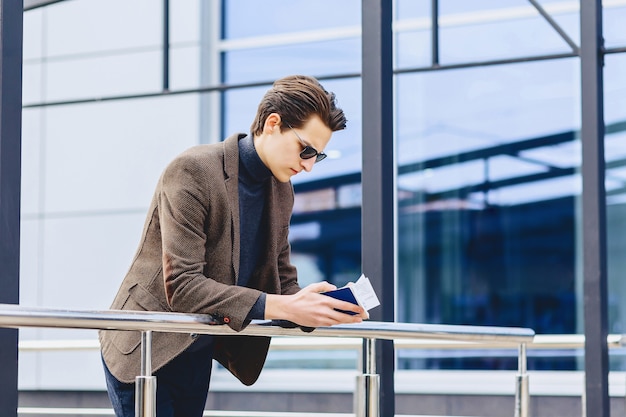 Stylish traveller in jacket with passport and tickets in urban context