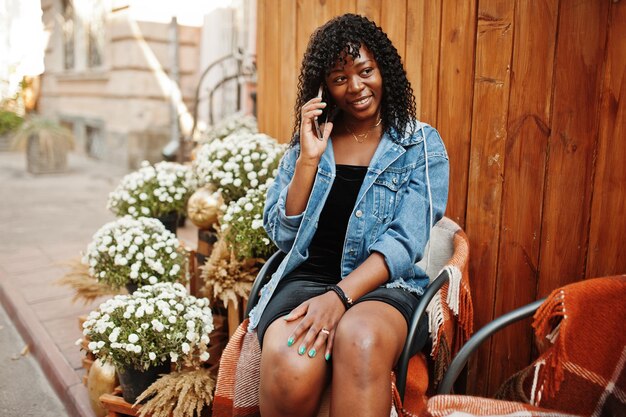 Stylish trendy afro france curly woman posed at autumn day in jeans jacket Black african female model with mobile phone