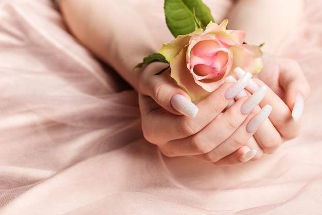 Стильный модный женский маникюр Красивые молодые женские руки с белым маникюром и розами на шелковом розовом фоне