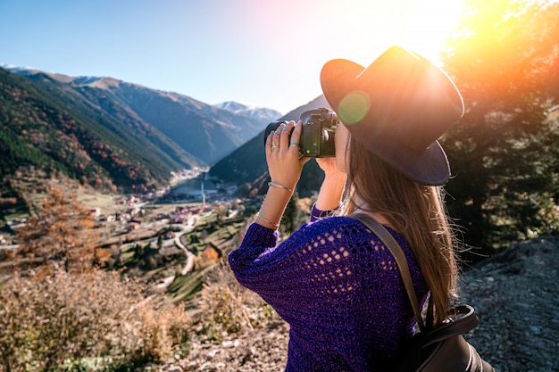 トルコ旅行中に山とトラブゾンのウズンゴル湖の写真を撮る茶色のバックパックとフェルト帽子のスタイリッシュな流行の流行に敏感な女性旅行者カメラマン