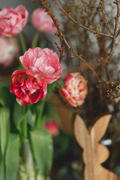 Stylish tulips and willow branches bouquet on background of easter decor on wooden table close up Happy Easter Rustic festive arrangement in dining room in farmhouse