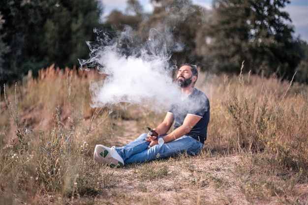 Stylish vaper smoking an vape on the forest ground. Smoking cessation tobacco.