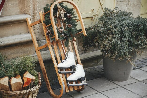 Stylish vintage ice skates and rustic wreath on wooden sleigh at building exterior Modern christmas decor in city street Winter holidays in Europe Merry Christmas