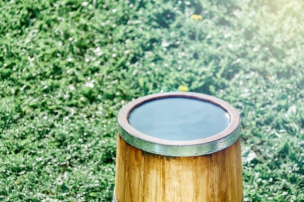 Stylish vintage oak wood tub with metal ring full of clear water stands on lush green lawn