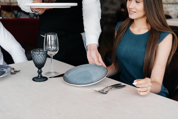 A stylish waiter in an apron serves a young girl in a fine\
restaurant and serves her a unique dessert covered with food gold\
exquisite delicacies of haute cuisine closeup