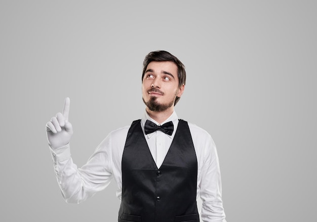 Stylish waiter in elegant uniform pointing up