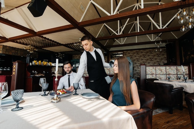 A stylish waiter serves a young couple of a man and a woman who
came on a date to a gourmet restaurant customer service in the
restaurant and catering establishments