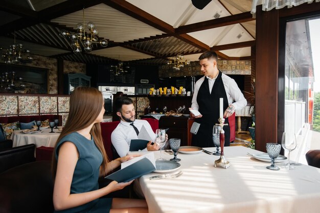 A stylish waiter serves a young couple who came on a date in a gourmet restaurant. Customer service in the catering.