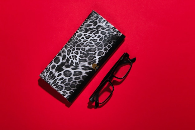 Stylish wallet and glasses on red with shadow.