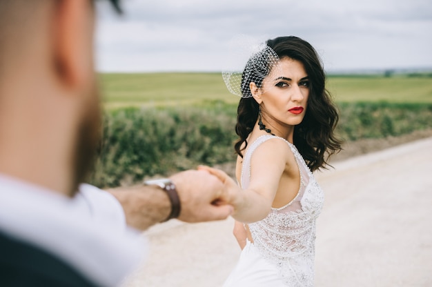 Stylish wedding couple walking on a field road near retro car