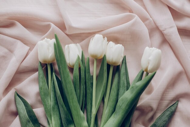 Stylish white tulips on beige soft fabric and rustic wooden table background top view hello spring flat lay soft light tenderness atmospheric moment space for text