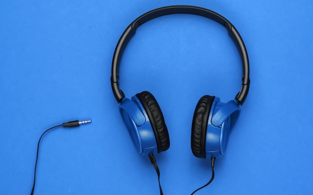 Stylish wired blue headphones on blue background. Music lover concept.