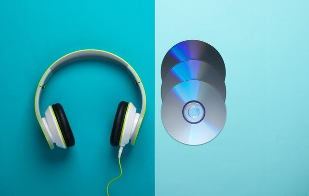 stylish wired stereo headphones and cd discs on blue surface