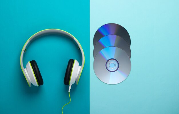 Stylish wired stereo headphones and cd discs on blue surface