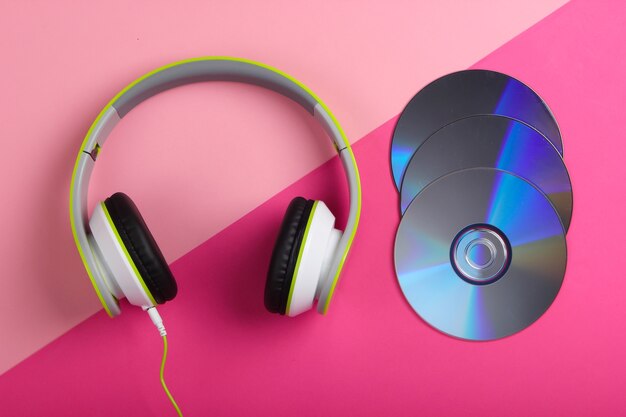 Stylish wired stereo headphones and cd discs on pink pastel surface