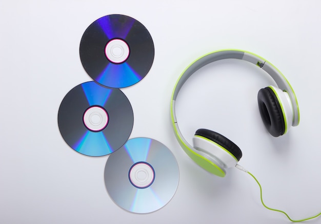 Stylish wired stereo headphones and cd discs on white surface