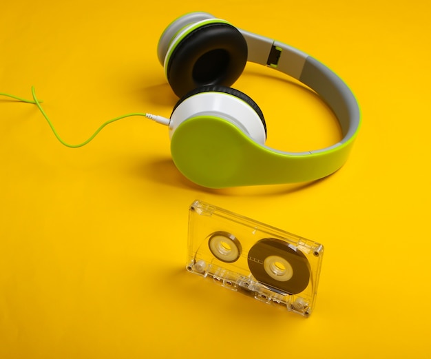 Stylish wired stereo headphones with audio cassette on yellow surface