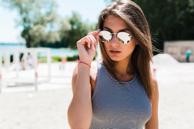 Стильная женщина, регулирующая солнцезащитные очки на пляже