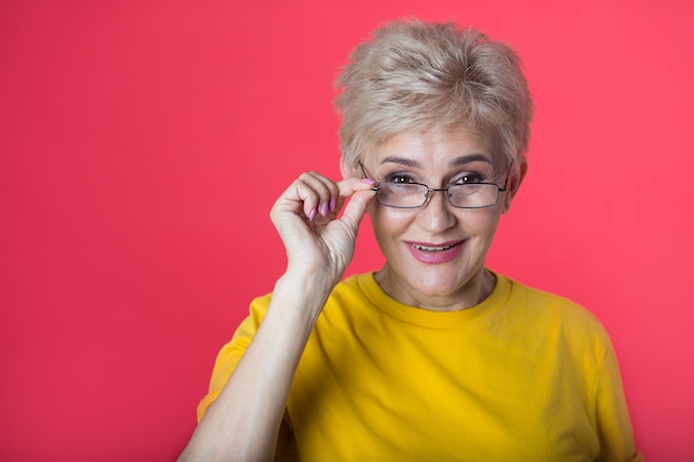 Photo stylish woman at the age with a short haircut in a yellow t-shirt on a red wall