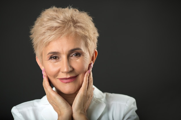 stylish woman aged with short hairdo in a white jacket on a black wall