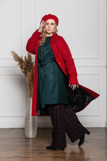 Foto donna alla moda in un berretto e cappotto su un muro chiaro.