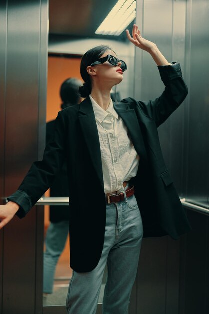 Стильная женщина в черной куртке и солнцезащитных очках позирует в модели лифта