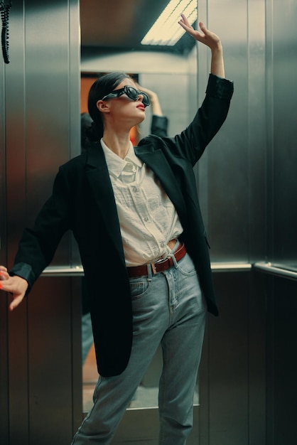 エレベーターのファッションモデルでポーズをとる黒いジャケットとサングラスを着たスタイリッシュな女性