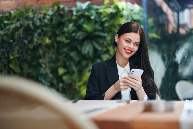 Photo stylish woman blogger sits in a cafe with a phone in her hands reads a message mobile communication and internet abroad video call freelance work online