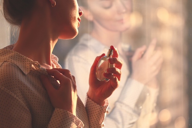 Photo stylish woman in blouse spraying a bottle of favorite perfume at sunset.