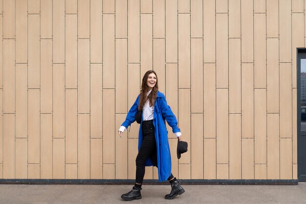 Stylish woman in a blue autumn coat walks around the city against the background of a beige wall