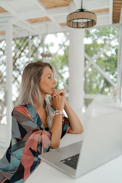 Stylish woman in bohemian outfit sitting in modern cafe and using lap top