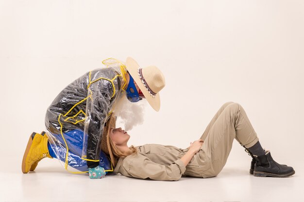 Stylish woman breathing out steam to man in the mask posing over white background