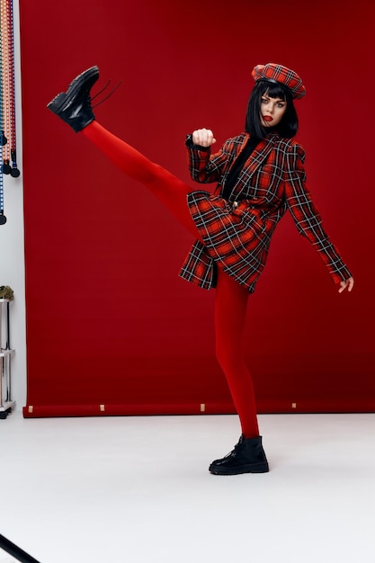 Stylish woman in a bright suit lifted her leg up on a red background