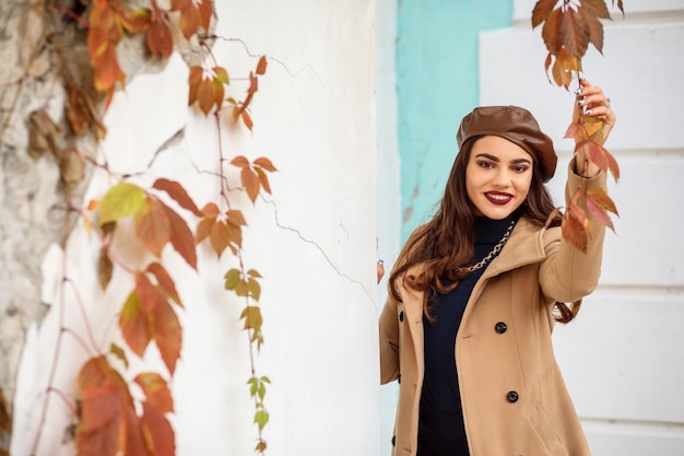 茶色の革のベレー帽とベージュのコートを着たスタイリッシュな女性は、秋のシーズンに屋外で時間を過ごしています