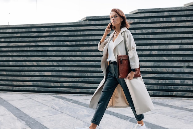 Stylish woman in a coat walking outdoors talking on a mobile phone