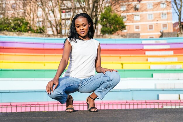 Stylish woman crouching confidently with a rainbow backdrop