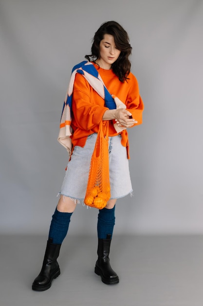 Stylish woman dressed in orange knitted jacket posing for a photo in a photo studio on a gray paper background Bright emotions poses modern concept