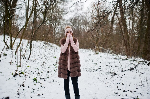 Stylish woman in fur coat and headwear at winter forest.